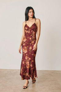 A flowing maroon satin floral chevron seam open back maxi dress with delicate gold beige floral pattern and mermaid silhouette