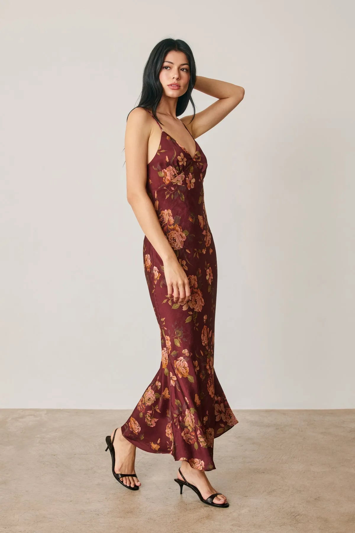 A flowing maroon satin slip dress with floral chevron seam pattern and thin straps featuring a flared hem