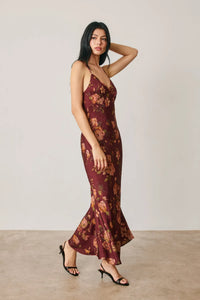 A flowing maroon satin slip dress with floral chevron seam pattern and thin straps featuring a flared hem