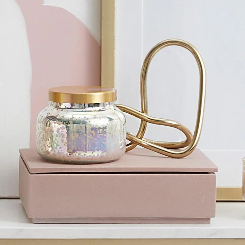 A mercury iridescent candle in a shimmering mercury glass jar with a gold lid and matching gold metal handle