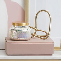 A mercury iridescent candle in a shimmering mercury glass jar with a gold lid and matching gold metal handle
