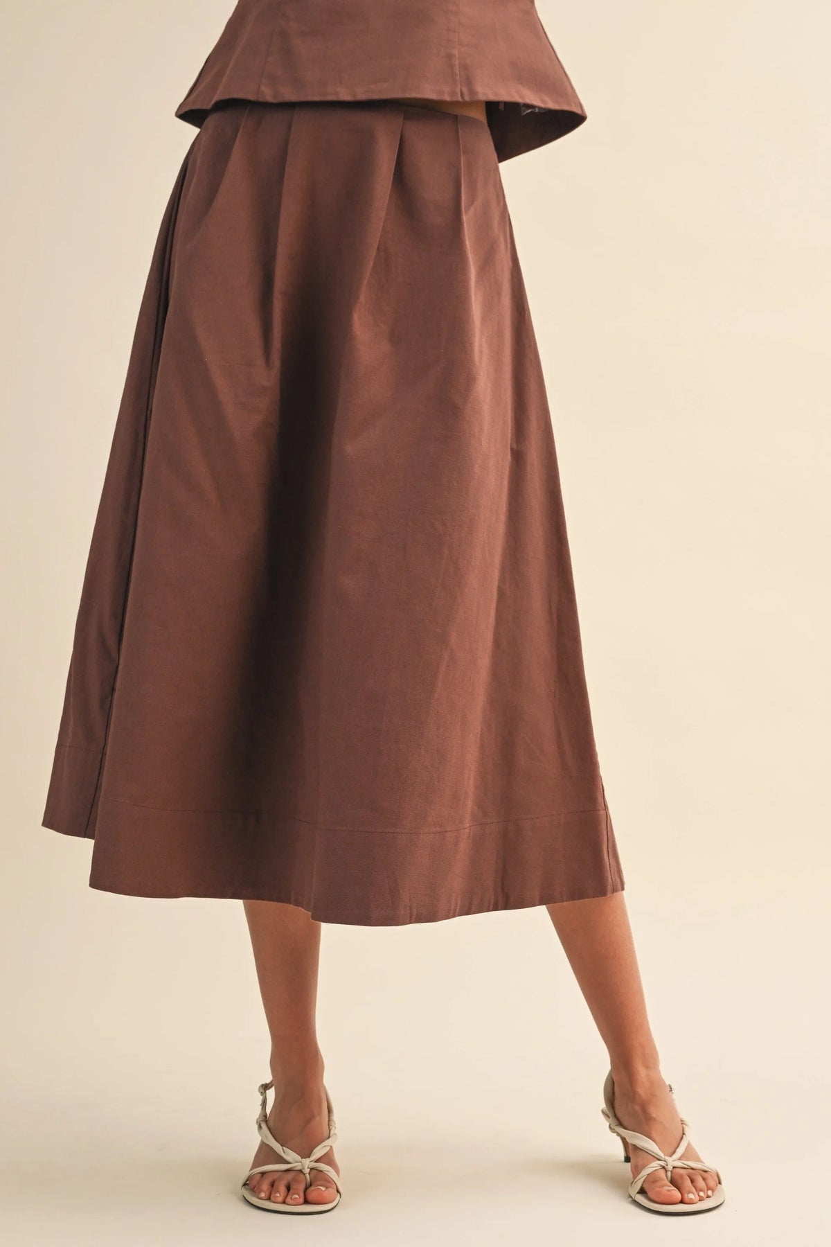 A flowing brown linen pleated waist flare midi skirt with matching top featuring a flared hem and mid-calf length