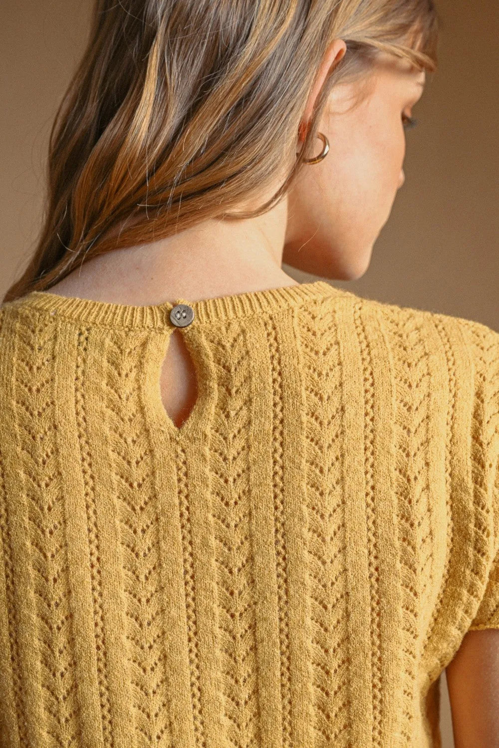 A mustard-yellow pointelle short sleeve knitted top with textured cable-knit pattern and button detail at neckline