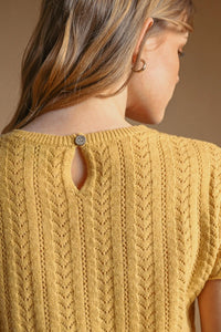 A mustard-yellow pointelle short sleeve knitted top with textured cable-knit pattern and button detail at neckline