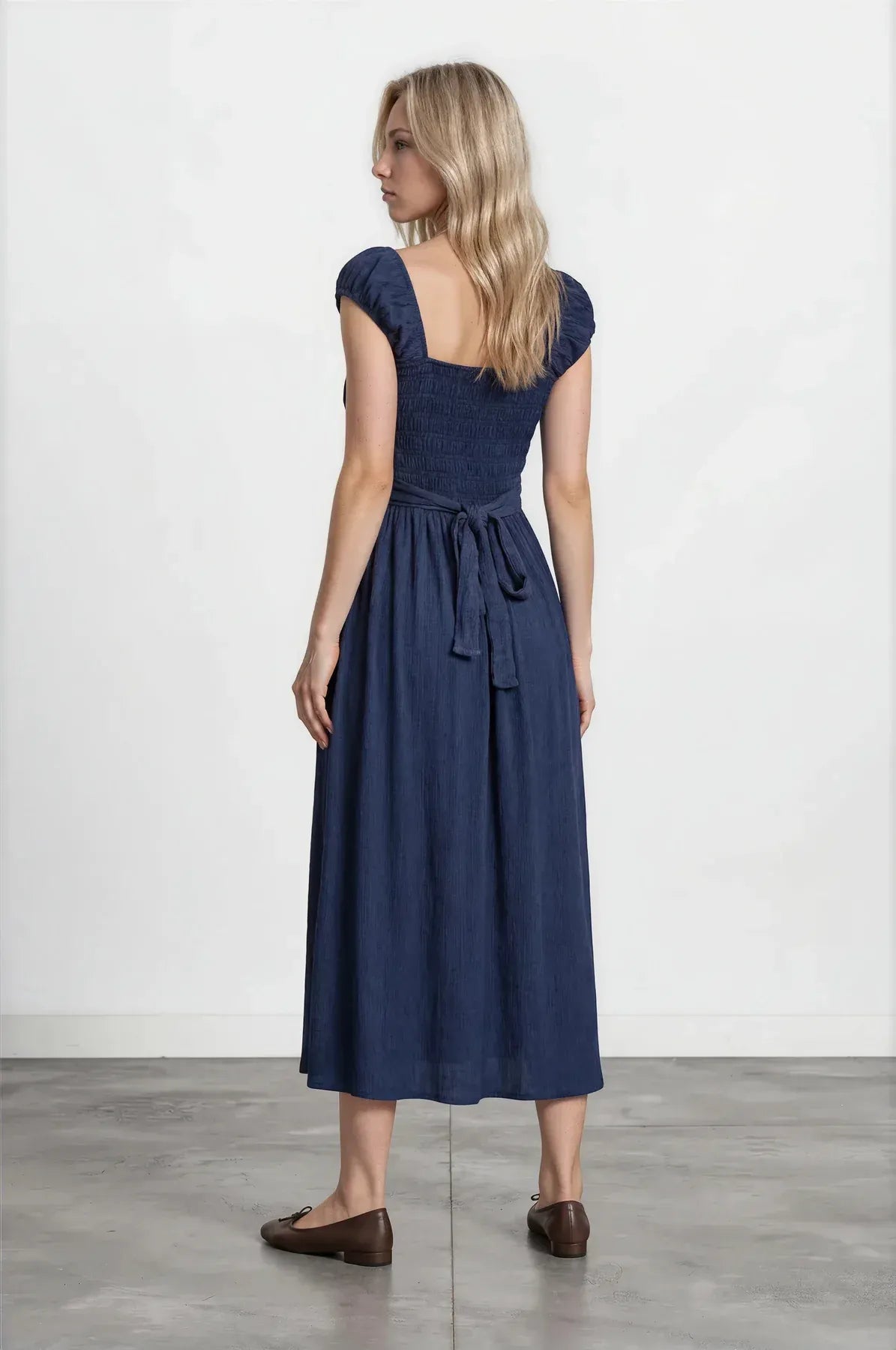 A navy blue sleeveless midi dress with square neckline and gathered waist tied with matching fabric belt smocked midi dress
