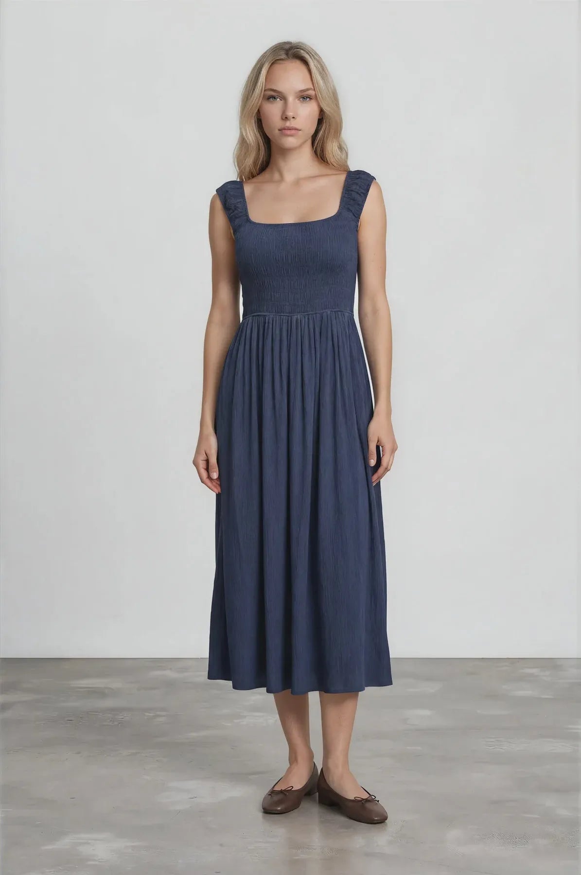 A navy blue sleeveless smocked midi dress with crinkle plisse fabric and ruffled shoulder straps