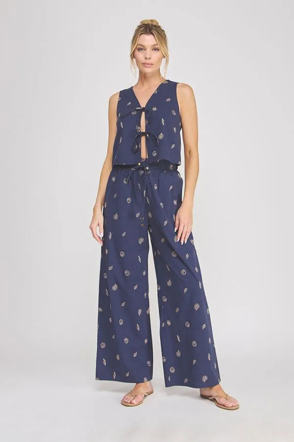 Navy blue sleeveless jumpsuit with subtle white floral pattern featuring seashell ruffle waist and elastic tie detail