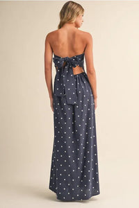 A navy blue polka dot tube maxi dress with strapless design and a back tie detail shown from the back side