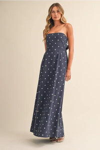 A navy blue polka dot tube maxi dress with a strapless fitted silhouette and tie back detail
