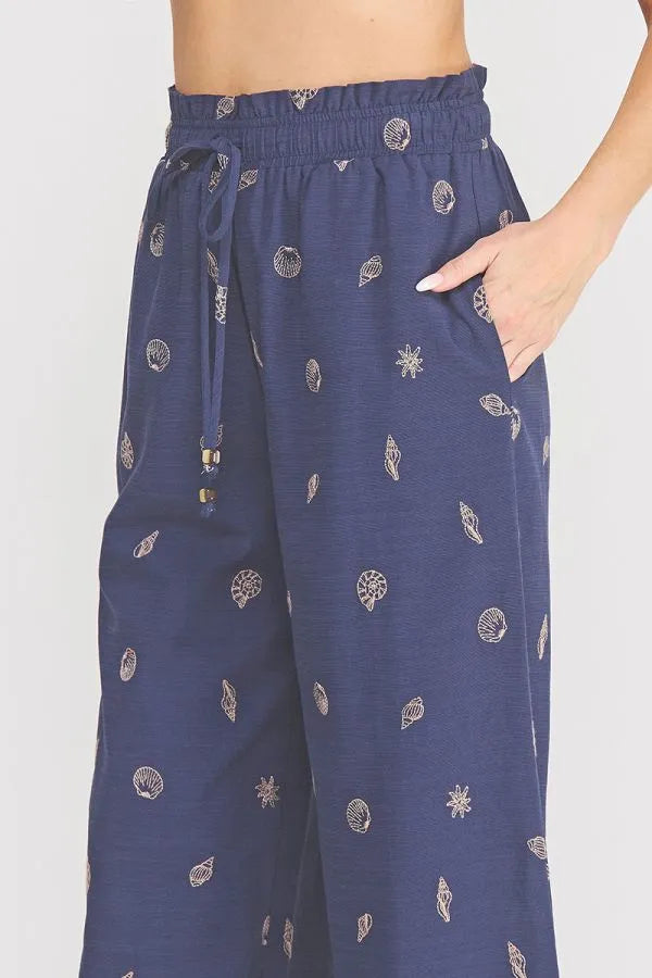 Navy blue wide-leg seashell ruffle waist pants with elastic tie waistband and white embroidered seashell pattern