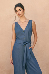 A navy blue sleeveless ocean current button jumpsuit with v-neckline, button-front closure, and self-tie belt