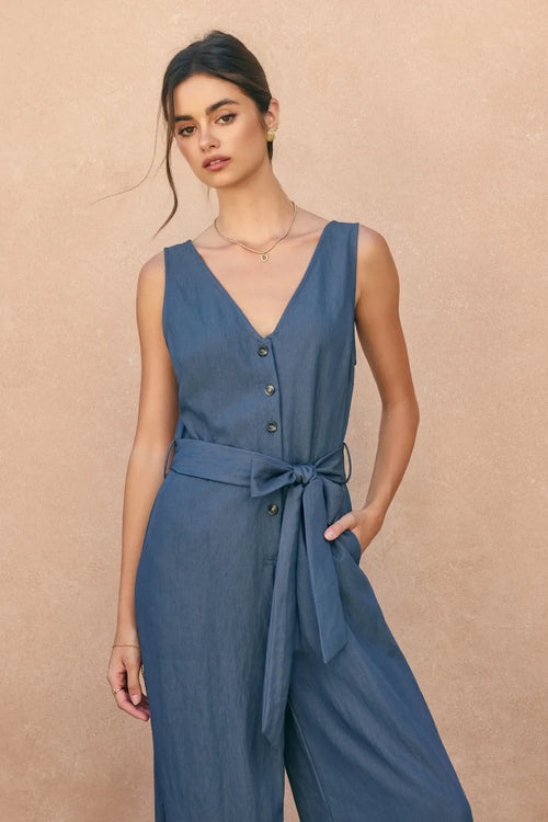 A navy blue sleeveless ocean current button jumpsuit with v-neckline, button-front closure, and self-tie belt
