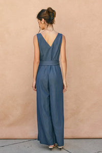 Back view of ocean current button down belt jumpsuit in sleek navy blue sleeveless design with deep v-back and matching belt