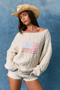 Off-the-shoulder cream cable-knit sweater with a textured american flag patch featuring a boat neck design