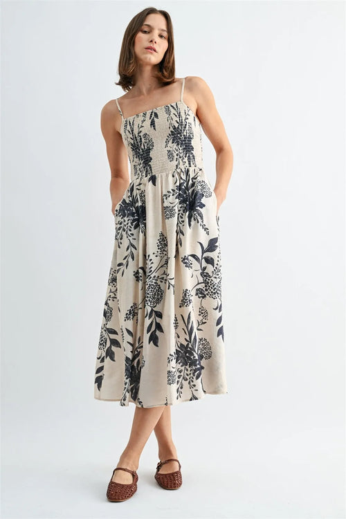 A flowing off-white midi dress with black botanical print and thin spaghetti straps smock design