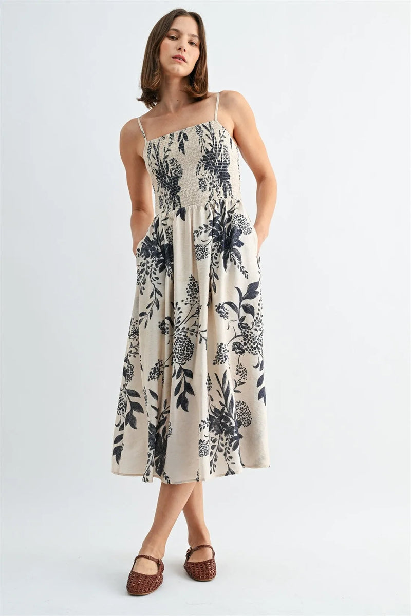 A flowing off-white midi dress with black botanical print and thin spaghetti straps smock design