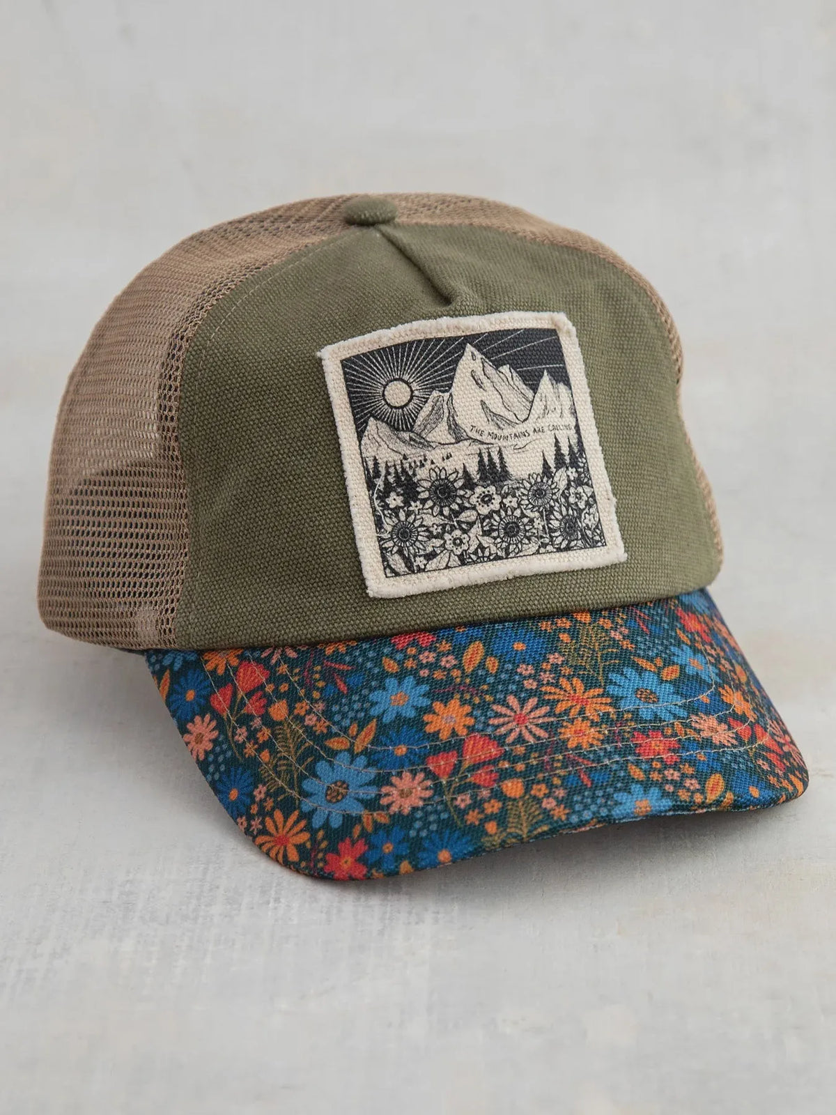 Olive green and tan mesh canvas trucker hat with a floral brim featuring blue orange and red blossoms mountains design
