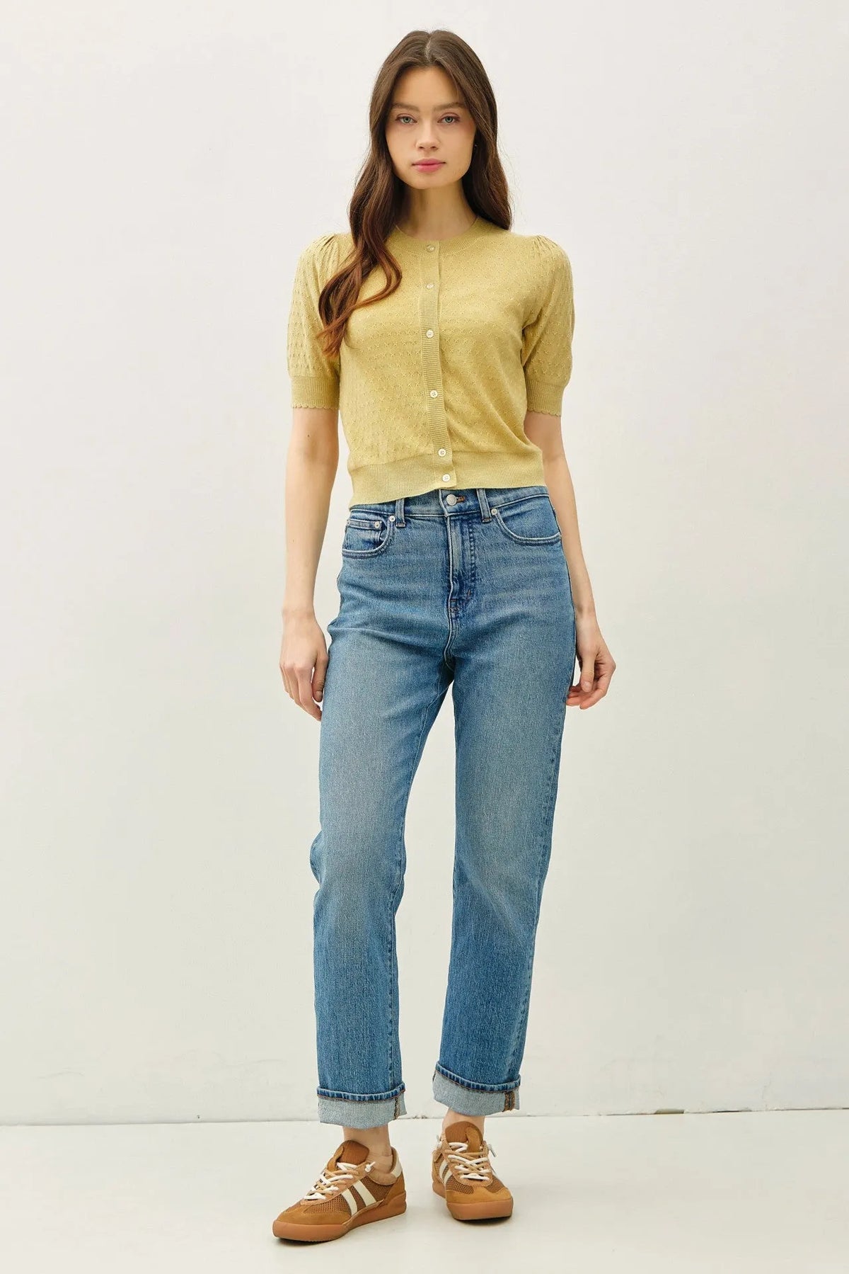 A pair of high-waisted blue denim jeans with rolled cuffs styled with a pointelle puff sleeve cardigan