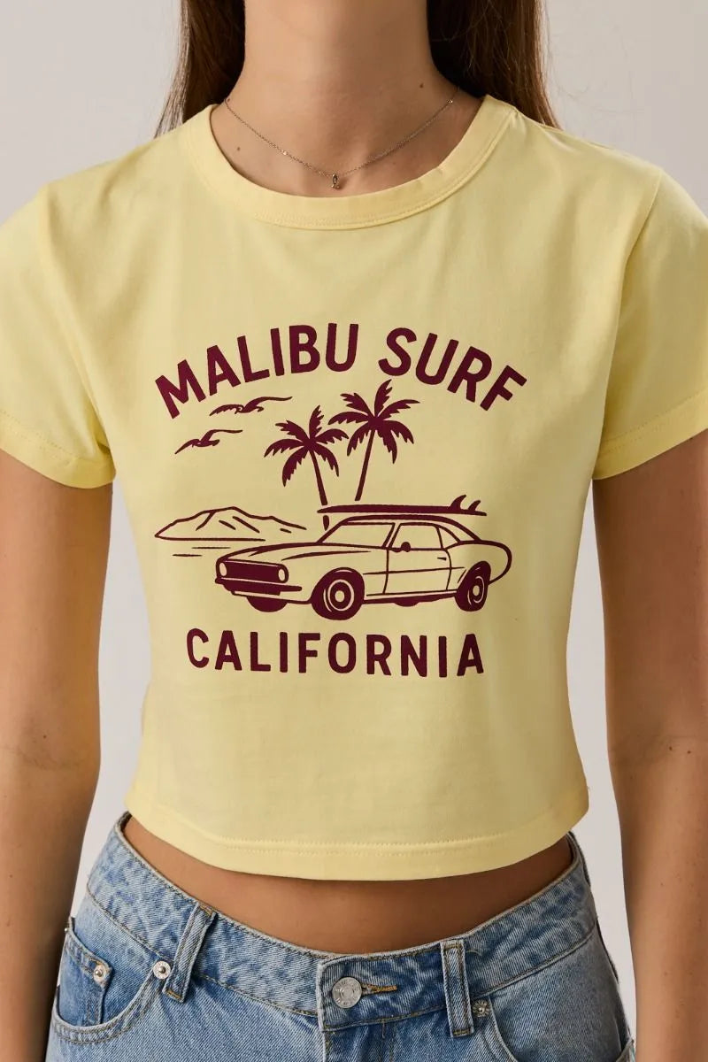 A pale yellow baby tee featuring a maroon malibu surf graphic with a vintage car and palm trees