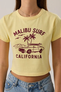A pale yellow baby tee featuring a maroon malibu surf graphic with a vintage car and palm trees