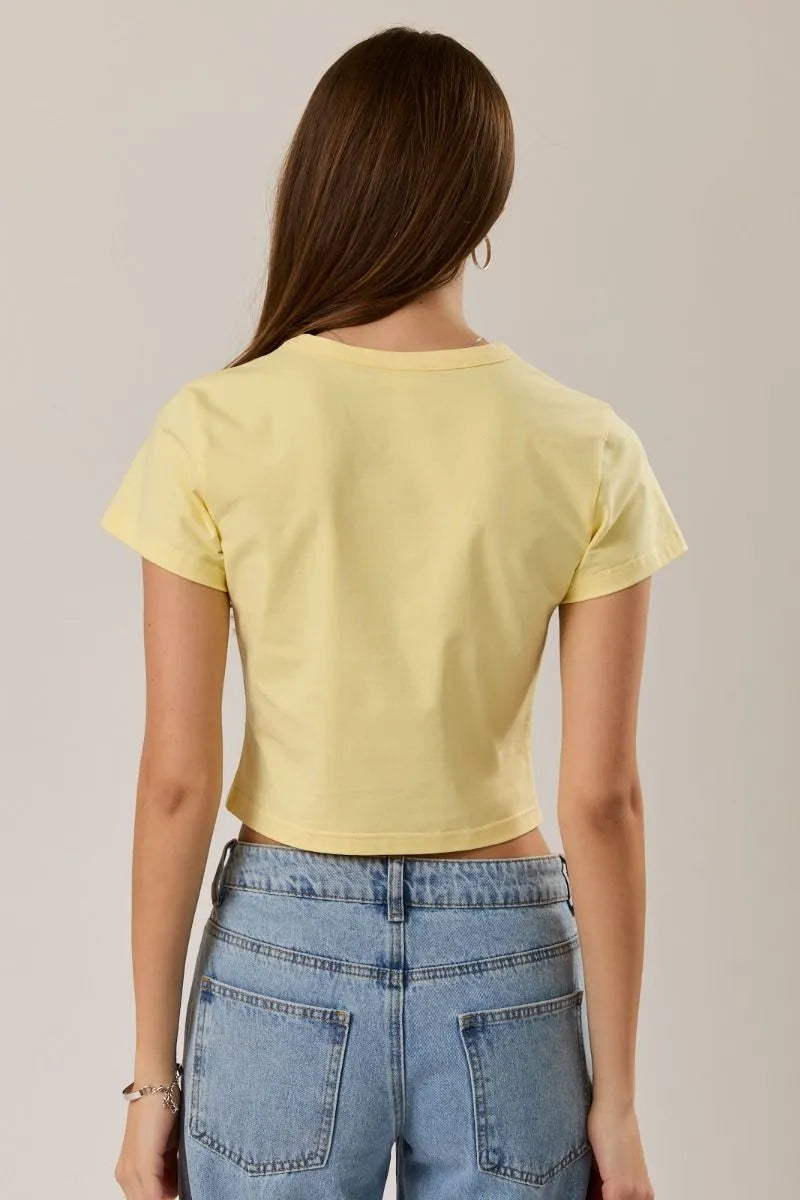 A pale yellow cropped t-shirt with short sleeves and round neckline featuring malibu surf graphic design