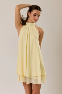 A flowing pale yellow halter neck ruffle hem mini dress with tiered hemline perfect for summer events