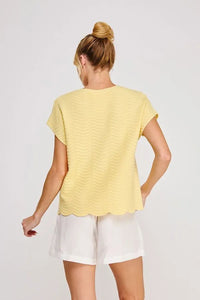 A pale yellow scallop pattern relaxed knit top with short sleeves and a scalloped hem in a wavy textured pattern