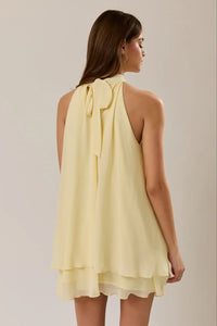 Pale yellow sleeveless halter neck ruffle hem mini dress with layered hem and tied bow at the back view