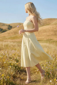 A flowing pale yellow sleeveless pleated a-line midi dress with fitted bodice and soft fabric