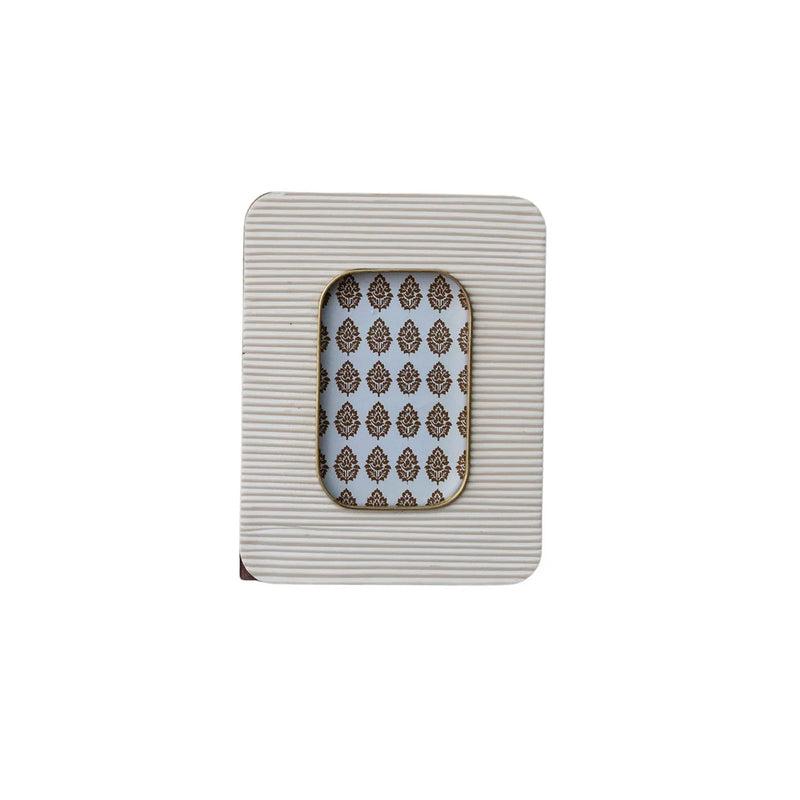 A rectangular white resin ribbed photo frame with brass inlay and an ornate brown damask patterned backing
