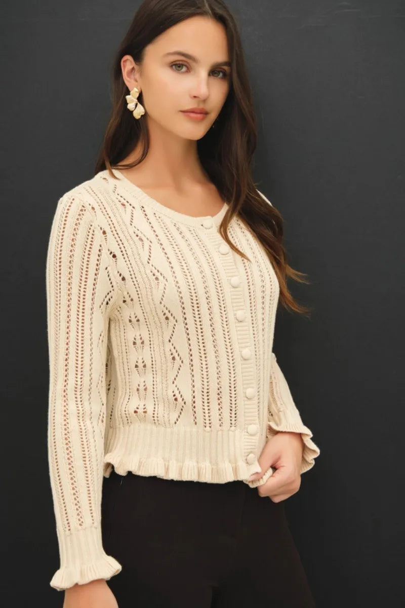 Cream-colored ruffled pointelle crop cardigan featuring intricate cable and lace knit with button closures and ruffled cuffs