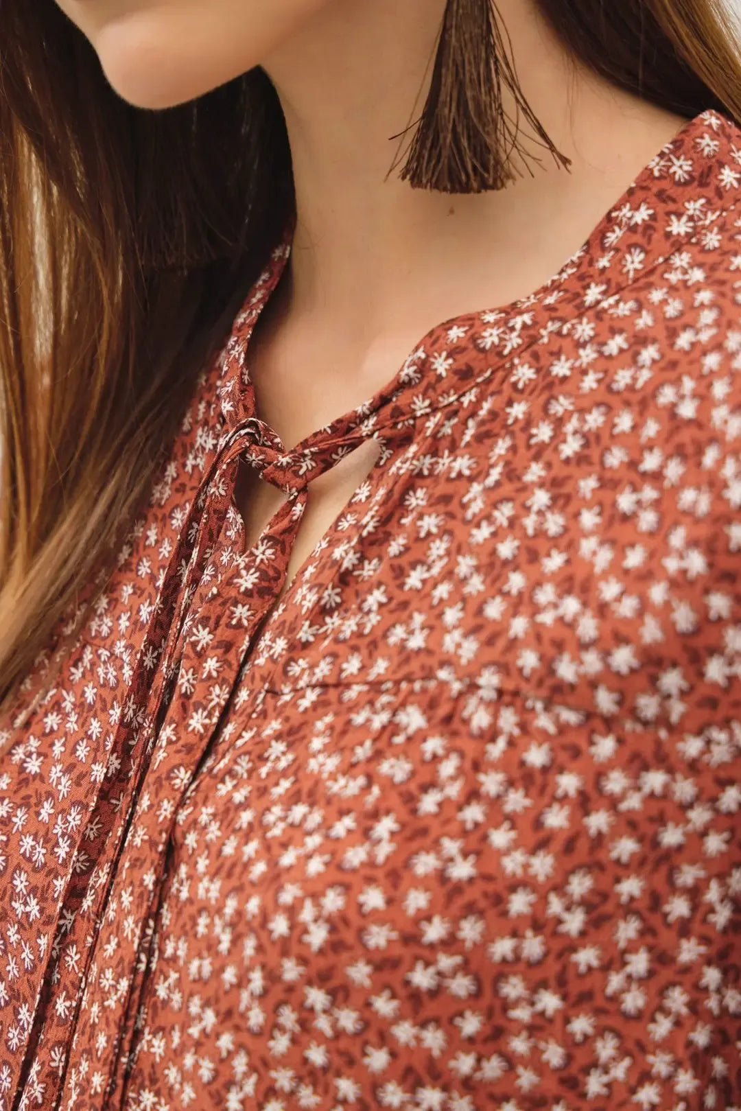 A rust-colored ditsy printed tie front collar blouse with delicate white floral pattern and tied neck detail