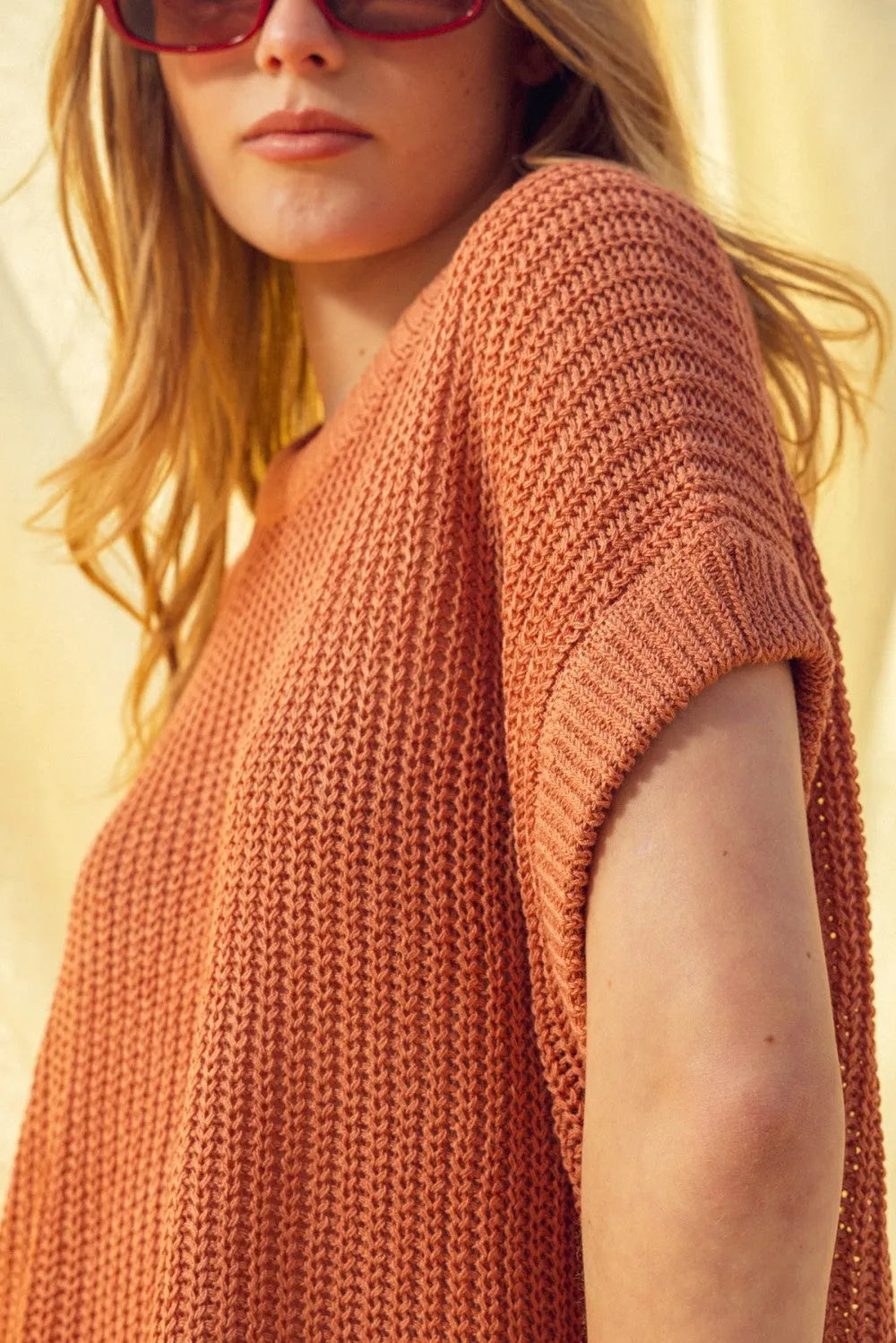 A rust-colored dolman sleeve knitted top with short sleeves and a relaxed fit in textured knit fabric
