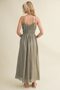 A flowing sage green linen maxi dress with a shirred bodice spaghetti strap and a gathered waist design