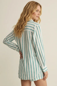A woman wearing a long-sleeved loose satin stripe button down shirt dress with vertical green and white stripes
