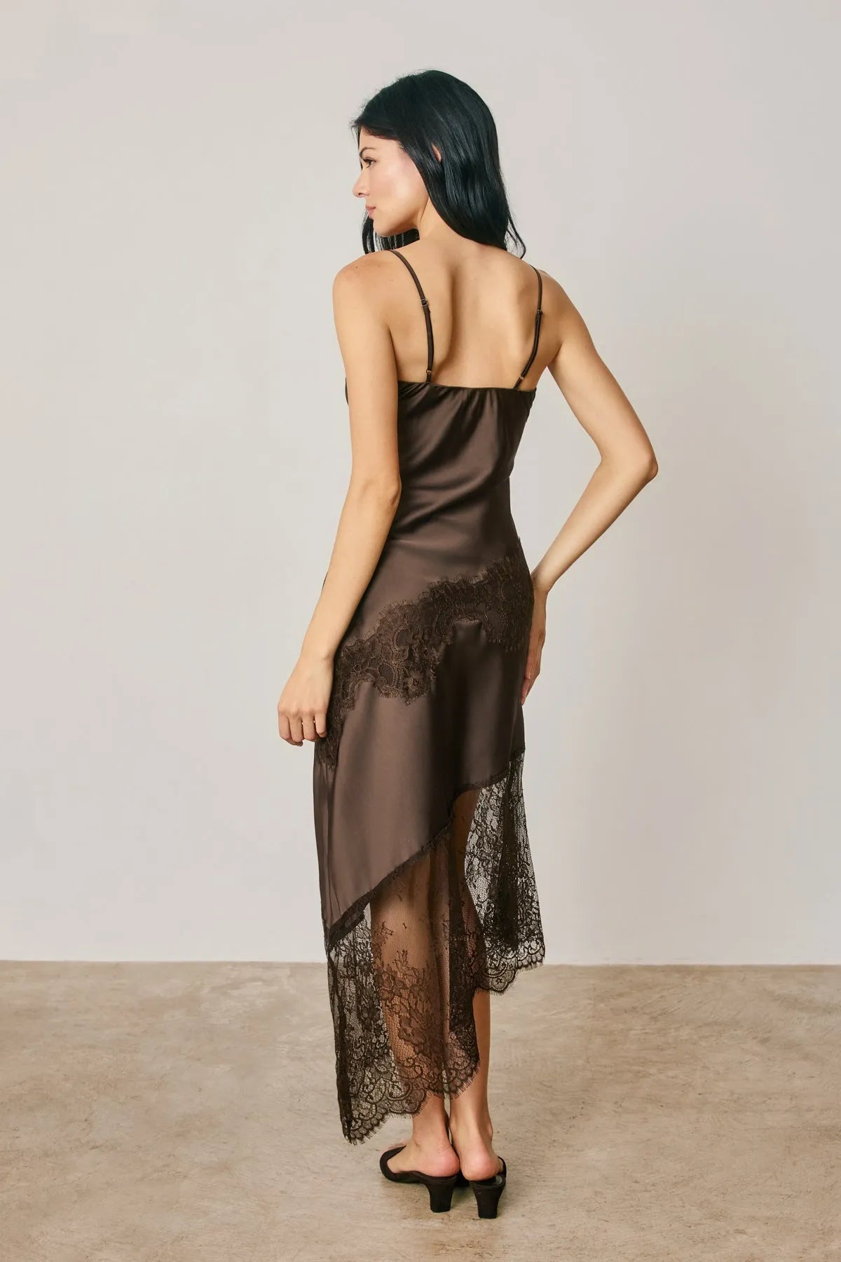 A sleek chocolate-brown satin midi slip dress with asymmetrical lace trim and delicate black lace accents