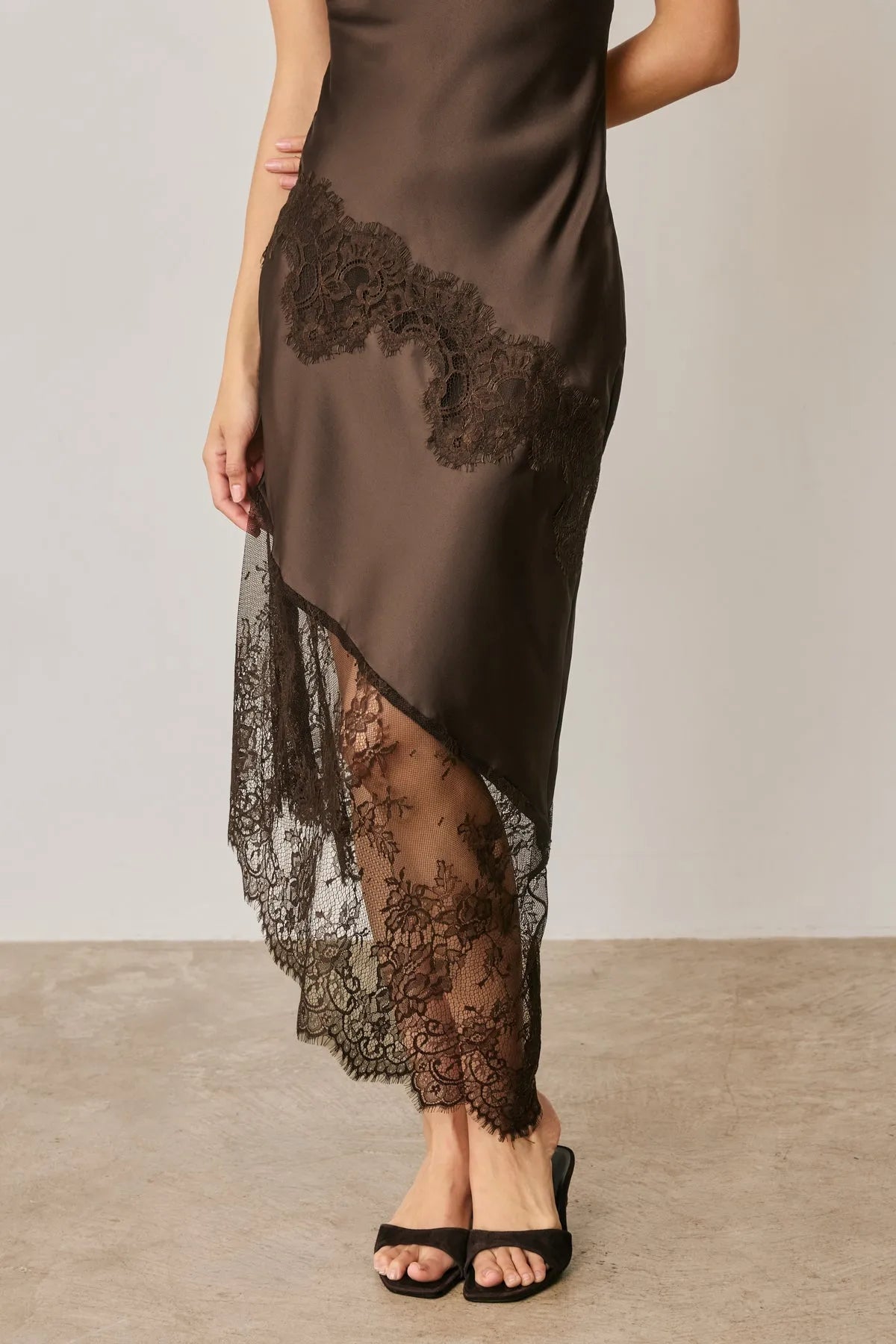 A sleek dark brown satin slip dress with asymmetrical lace trim and intricate black lace detailing on side and hem