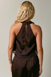 Back view of a sleek dark brown satin halter neck jumpsuit with delicate black lace trim along the lower back