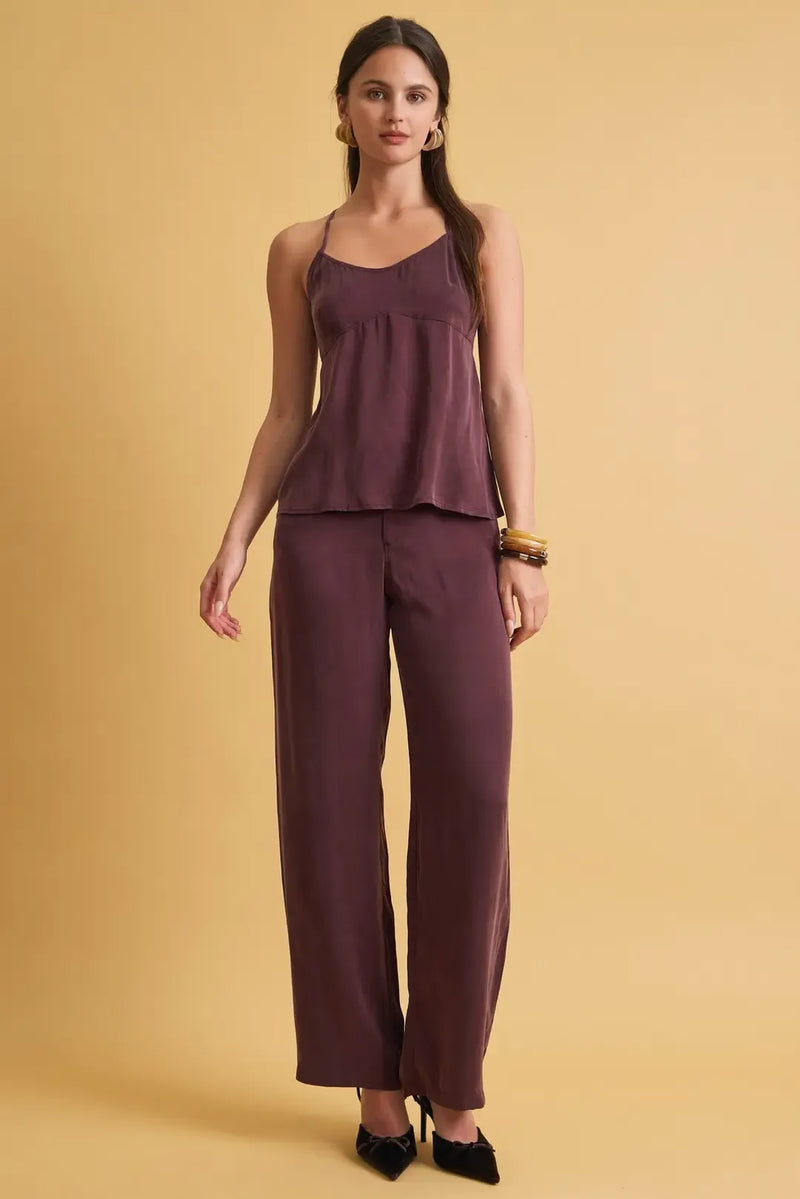 A sleek deep purple satin camisole with ruffled hem and thin straps paired with loose fit wide leg pants
