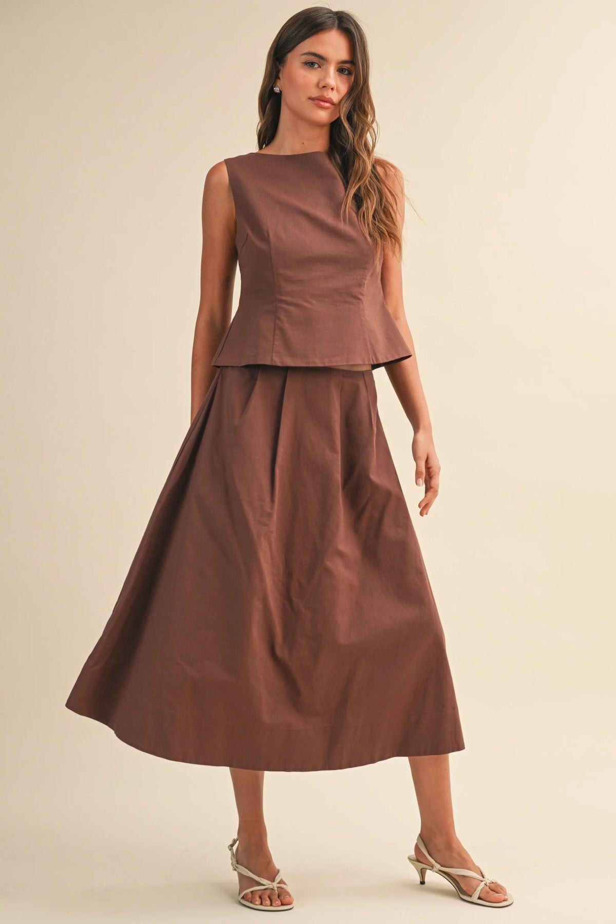 A sleek brown satin two-piece featuring a linen sleeveless peplum top and a flowing midi skirt