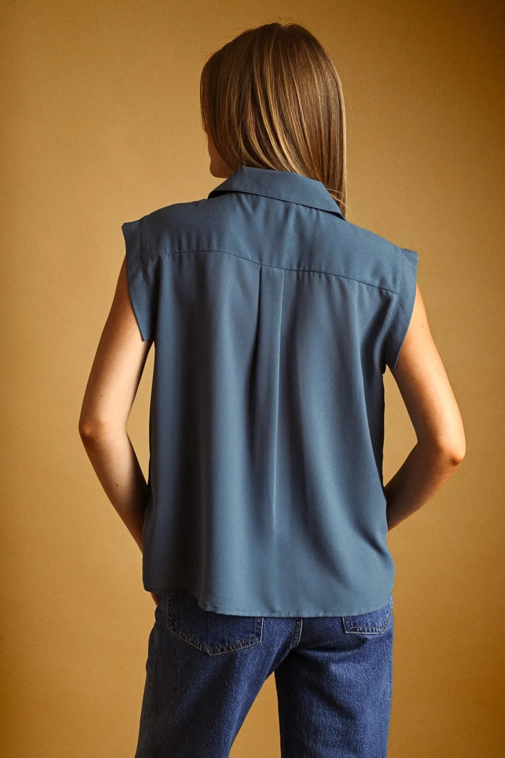 Blue sleeveless chiffon blouse with front pocket button and subtle pleats at the back in soft flowing fabric