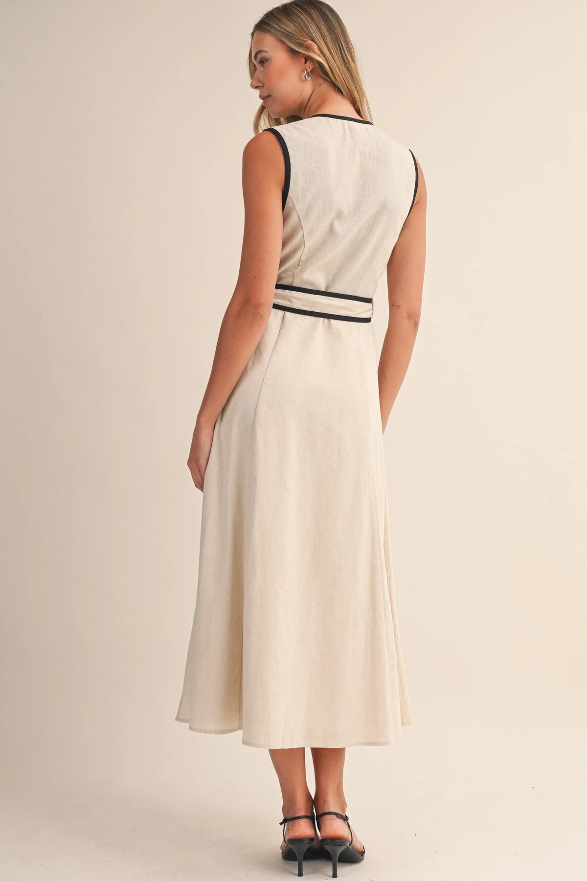 A sleeveless cream-colored midi dress featuring contrast piping wrap details along the neckline and waistband