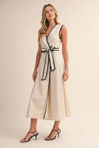 A sleeveless cream-colored midi dress with contrast piping wrap detail along neckline and waistband