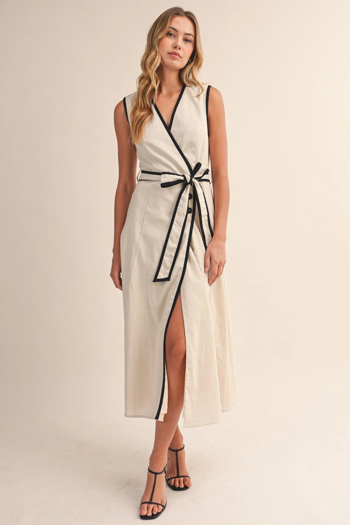 A sleeveless cream contrast piping wrap midi dress with black trim along the neckline waistband and side slit