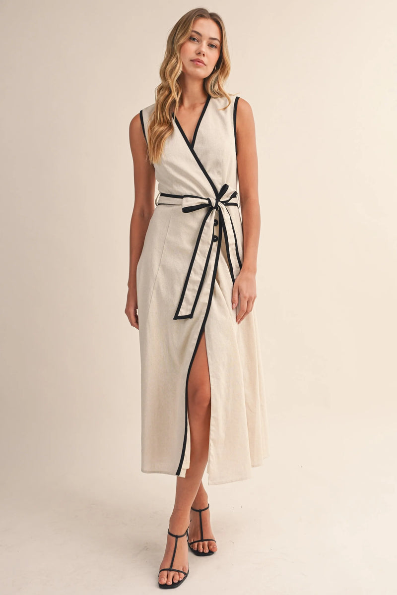 A sleeveless cream contrast piping wrap midi dress with black trim along the neckline waistband and side slit