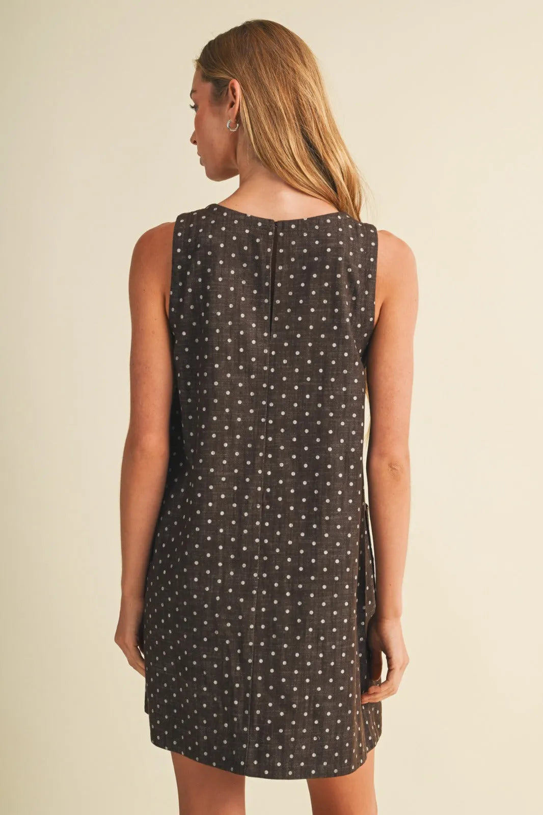 Back view of a dark gray polka dot sleeveless mini dress with a simple seam and slightly flared hem