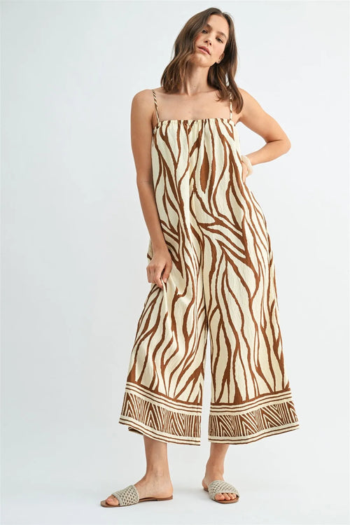 A flowing sleeveless border print jumpsuit featuring a bold brown and cream zebra print pattern