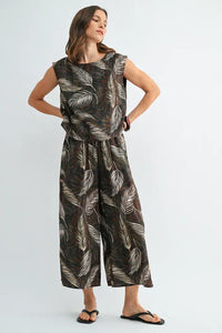 A flowing sleeveless jumpsuit with a dark brown base and white leaf print wide shoulder design