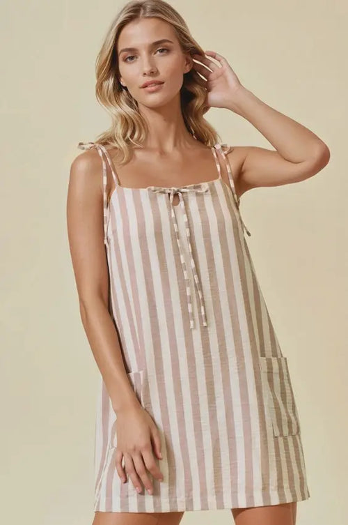A sleeveless knee-length stripe cotton gauze mini dress in beige and cream with adjustable tie shoulder straps and front pockets