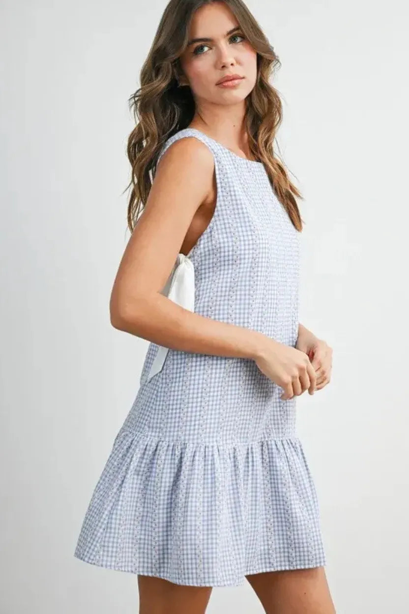 Sleeveless light blue and white gingham flounce mini dress with ruffled hem and back tie detail showing the back side
